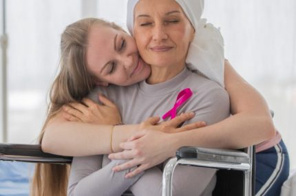 A middle-aged breast cancer woman with clothing around her head effected from chemo therapy sitting on wheel chair and hold hand of her daughter with hope and trust in love.
